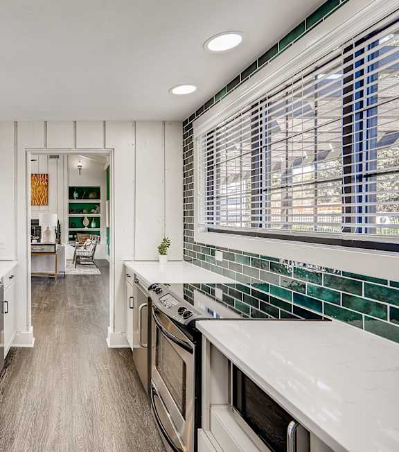 A kitchen with white cabinets and a green tile backsplash.