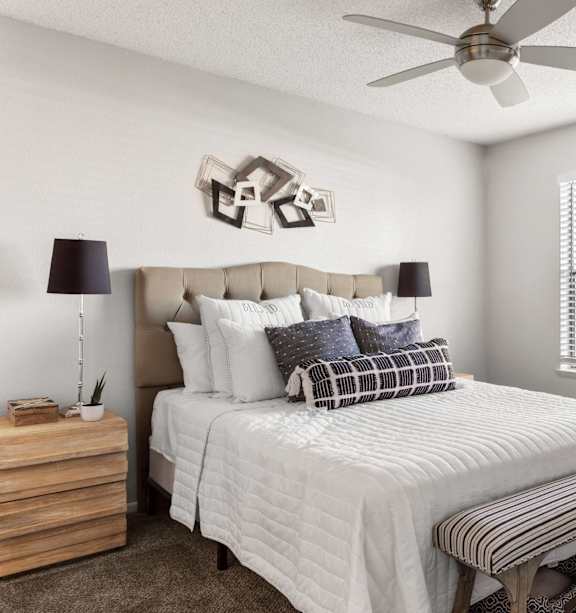 A bedroom with a bed, a bench, and a ceiling fan.