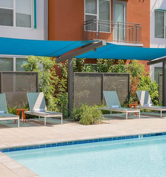 A pool with a blue canopy and lounge chairs.