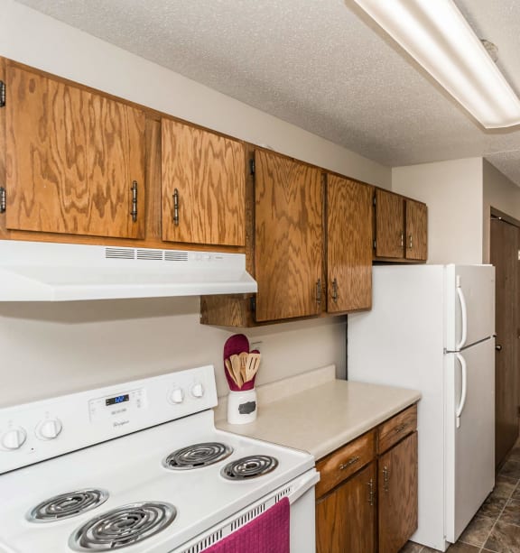 Grand Forks, ND Library Lane Apartments. A kitchen with a white refrigerator freezer next to a stove top oven