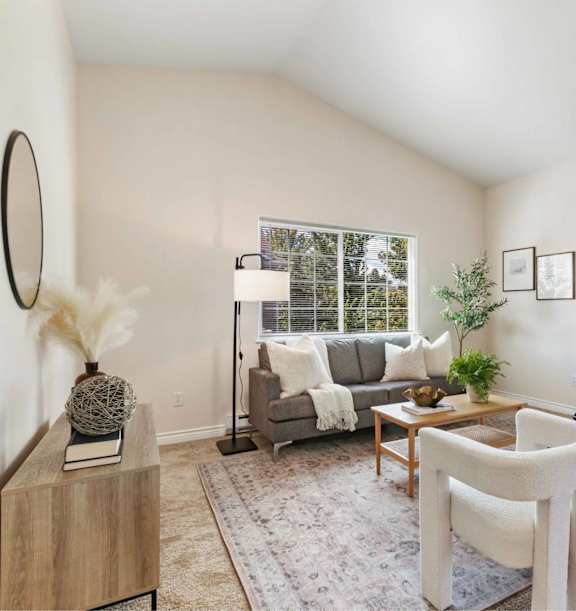 A living room with a grey couch, a wooden coffee table, and a large window.