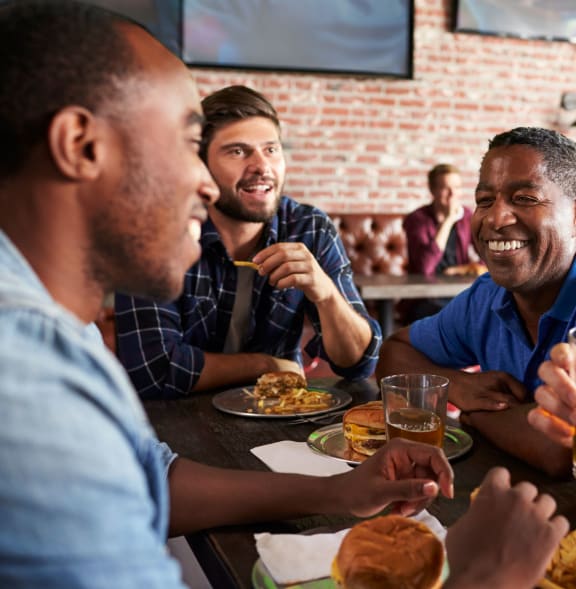 a group of men sitting around a table eating food and drinking beer