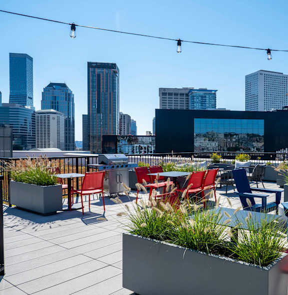 A rooftop patio with red and blue chairs and tables overlooking a city skyline.