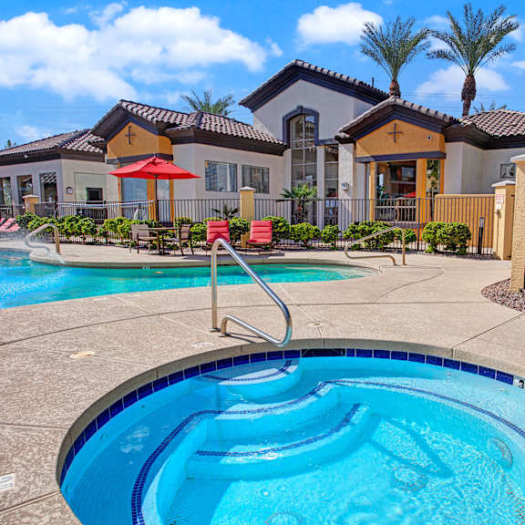 A hot tub with a pool in the background, surrounded by a gate, with pool chairs nearby, at Sonoma Landing.  