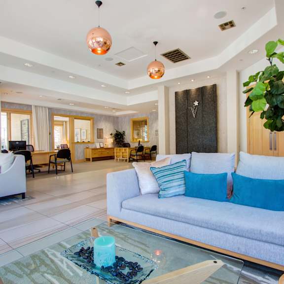 A clubhouse with a blue couch, plush blue chairs, and a glass table at Vesada Apartment Homes. 