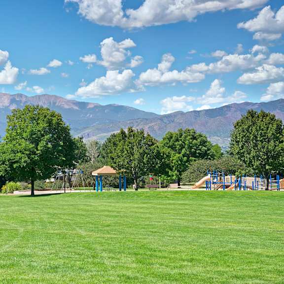A park with a playground and mountains in the background at Windtree Apartment Homes. 