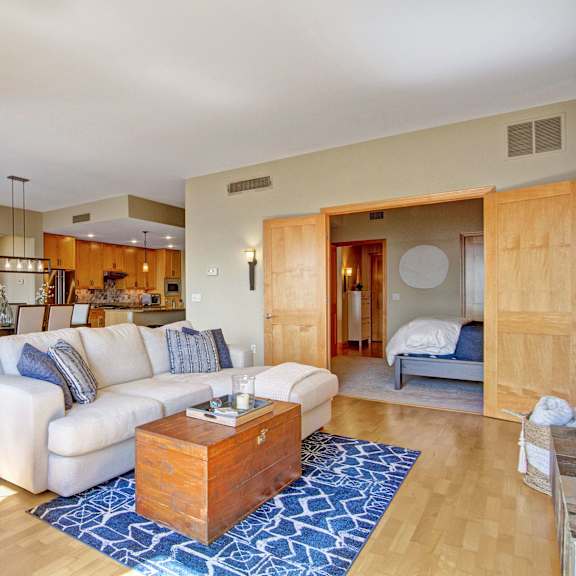 The Mist Living Room The spacious living room with a white couch, a blue rug, brown leather plush chairs, coffee table, overhead lighting, decorations, and view of the dining room with a table, chairs, and the kitchen at the Mist at Lake Minnetonka Apartment Homes.