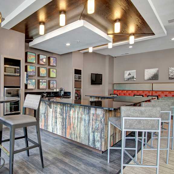 The clubhouse with barstool chairs, countertops, tall tables, artwork, a coffee station, and a TV at Residence at the COR. 