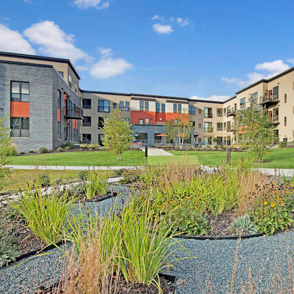 Siena Exterior The large, grassy area with a pathway and trees behind the apartment buildings at Siena Apartment Homes.