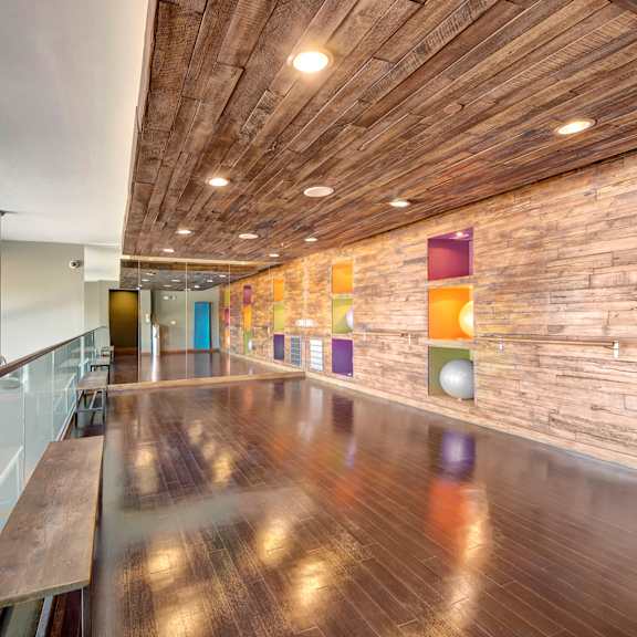 The yoga room with a glass railing, a wood floor, wood benches, and colorful exercise balls stored in the walls.  