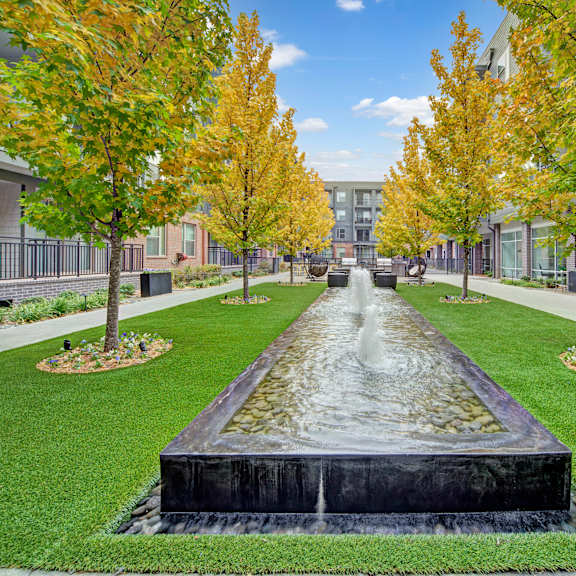 A fountain in the middle of a grassy area with trees the Metropolitan