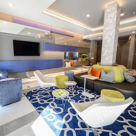 Harmony Luxury Apartments entertainment room with tall ceilings A resident lounge with a TV, tables, chairs, and benches at Harmony Luxury Apartments.