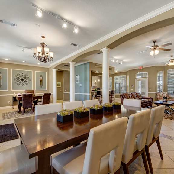 The resident lounge with couches, decorations, plush chairs, windows, coffee tables, and French doors to the pool area at Mission Green Apartments. 