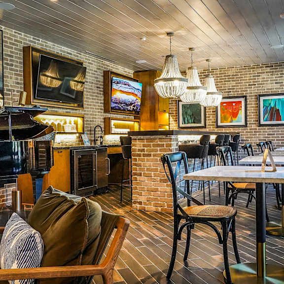 The Crosby at The Brickyard vibrant social space The resident lounge with brick walls multiple small tables a green velvet chair, a grand black piano, wall artwork, mini chandeliers, a community kitchen with a bar at the Crosby at the Brickyard Apartment Homes.
