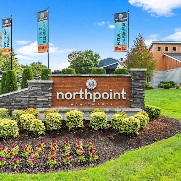 A sign for Northpoint Apartments is surrounded by flowers and greenery.