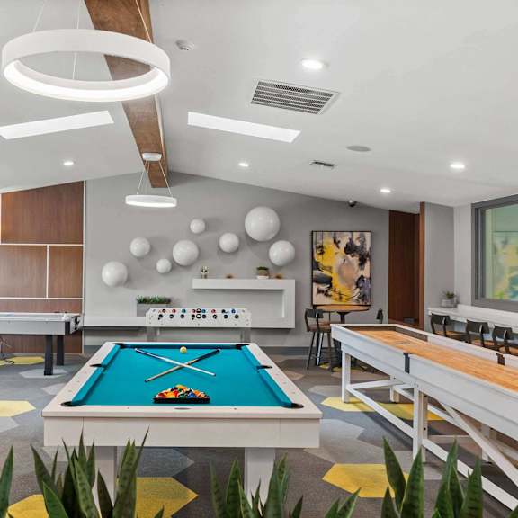 A pool table is in the middle of a room with a shelf and a painting on the wall.