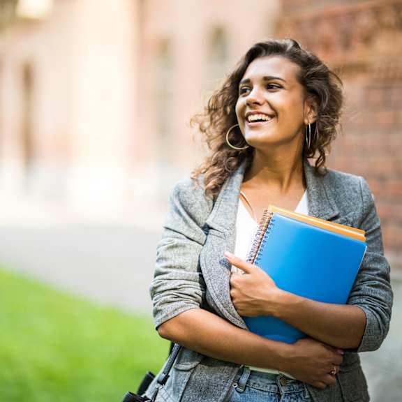 portrait of a smiling young woman holding books and cell phoneat OSM Properties Homes & Apartments, Chico