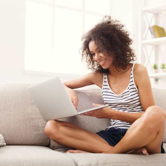A woman is sitting cross-legged on a couch using a laptop.