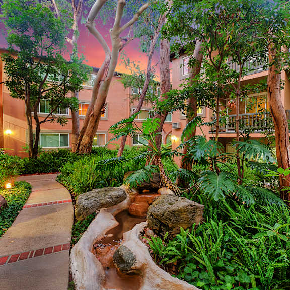 A garden with a waterfall and a building in the background.