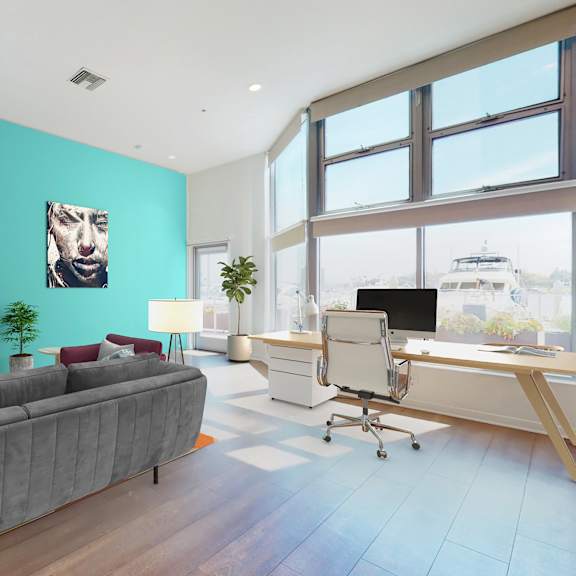 A modern living room with a grey sofa, a television, and a desk with a chair.