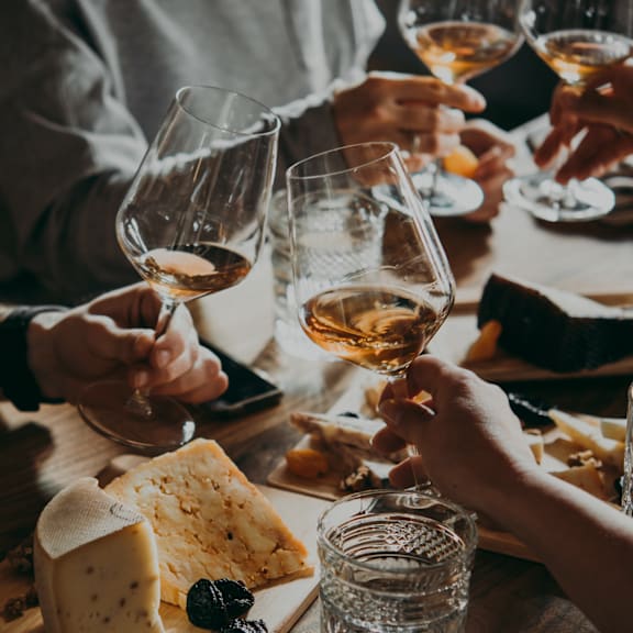 A group of people toasting with glasses of wine at a cheese board.