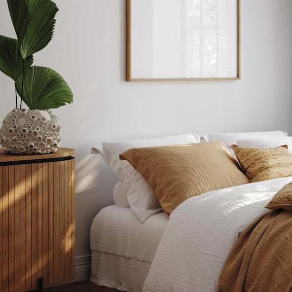 A white bed with brown pillows underneath a white picture frame on the wall.