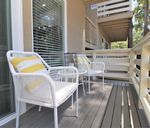 a porch with white wicker chairs and a yellow and white pillow