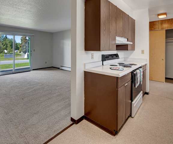 A kitchen with a stove and a refrigerator next to an empty living room at Bay Arms Apartments. 