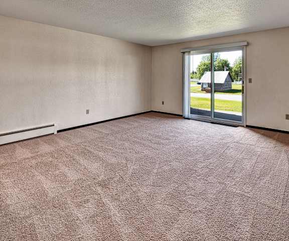 An empty living room with a sliding glass door to a yard at Bay Arms Apartments.