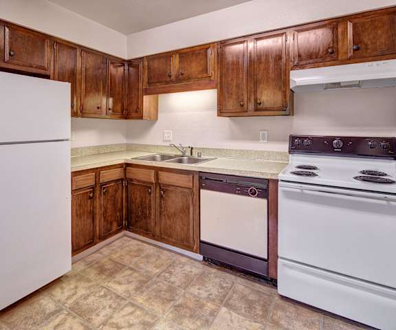 A kitchen with white appliances and counters with wooden cabinets at Castle Apartments. 