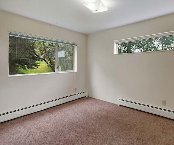 An empty, carpeted bedroom with two windows at Chugach South Apartments. 