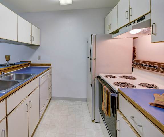 A kitchen with white cabinets, blue counters, and a sink and a refrigerator at Chugach South Apartments. 