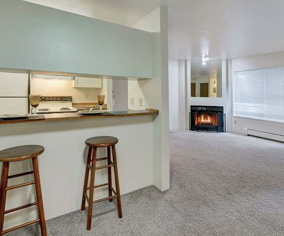 The living room and kitchen with a fireplace and bar stools at Chugach South Apartments.