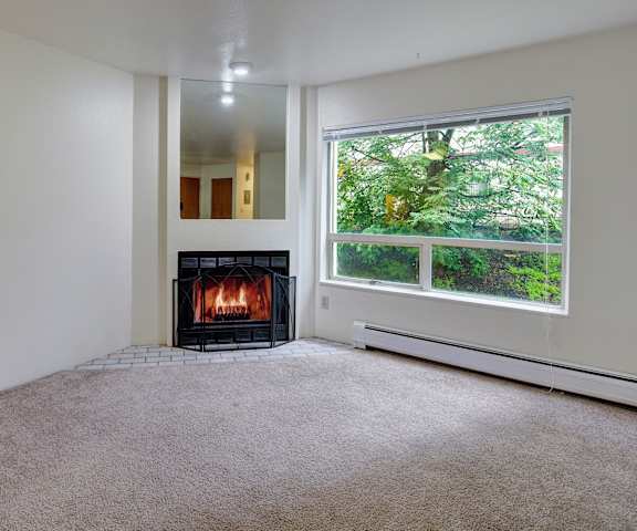 A living room with a fireplace and large window with a view of trees at Chugach South Apartment Homes.