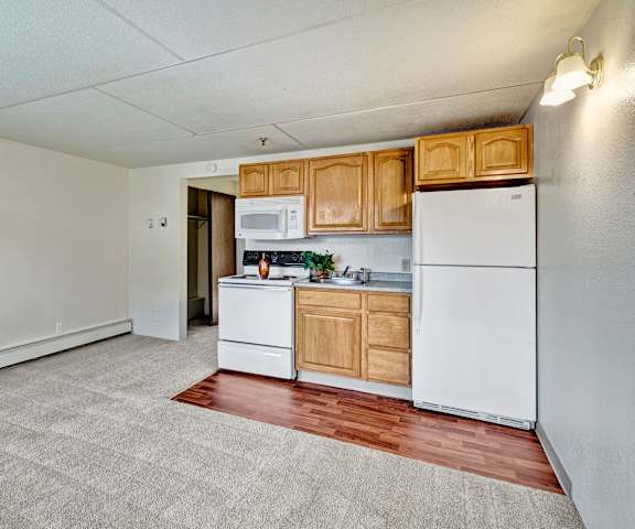 An empty living room with carpeting and kitchen at College View Apartments. 