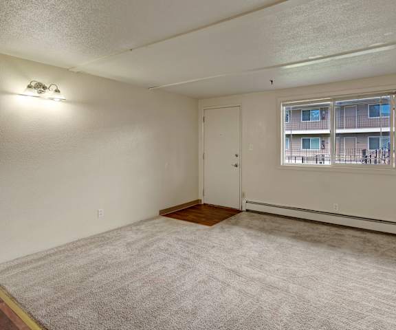 An empty living room with carpeting and a door to the front at College View. 