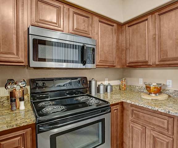 A large, modern kitchen with stainless steel appliances, kitchen utensils, granite countertops with lots of room, and large wooden cabinets at the Hawthorne Apartment Homes. 