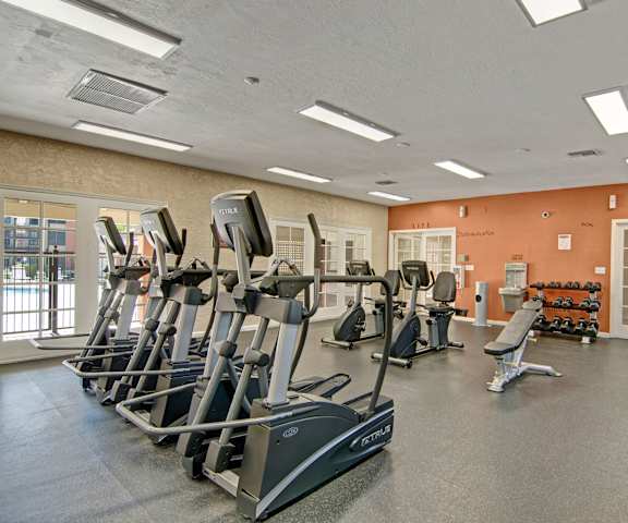 A gym with cardio machines, windows, TVs, and weights at Motif Apartments. 