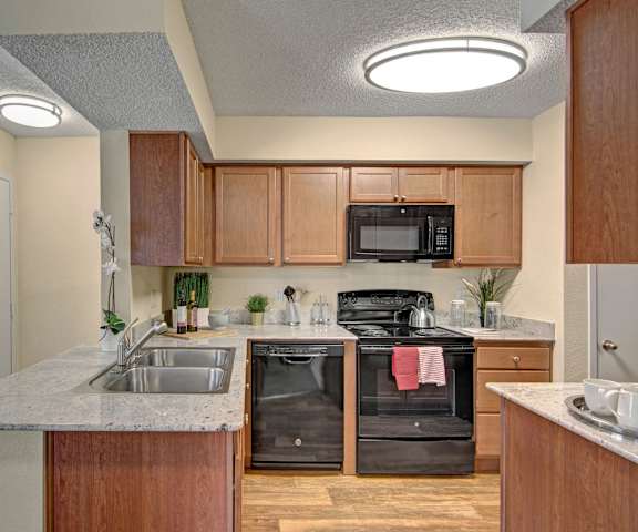 A large kitchen with black appliances, marble countertops with ample space, and spacious wooden cabinets with decorations at Motif Apartments. 