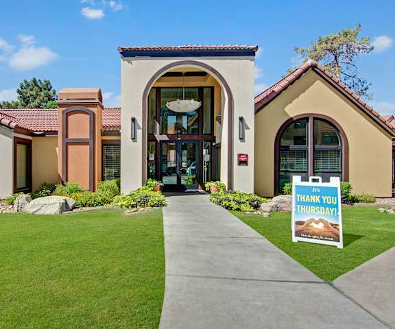 The exterior entry to the tan and orange colored front office building surrounded by plants and grass at Motif Apartments. 