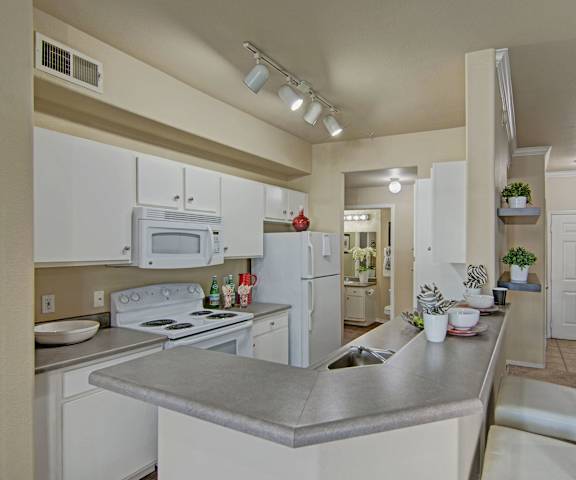 A large kitchen with white appliances, light counter with ample space, and spacious wooden cabinets at Mozaic at Steele Park Apartments. 