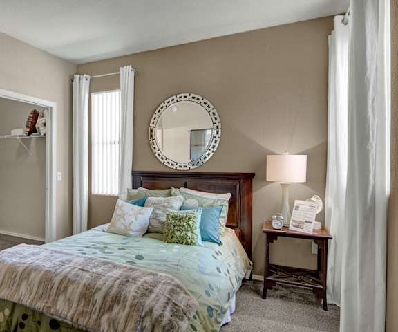 A bedroom with a queen-size bed, a dresser, decorations including a mirror, closet, and nightstands at Pala Mesa Apartments. 