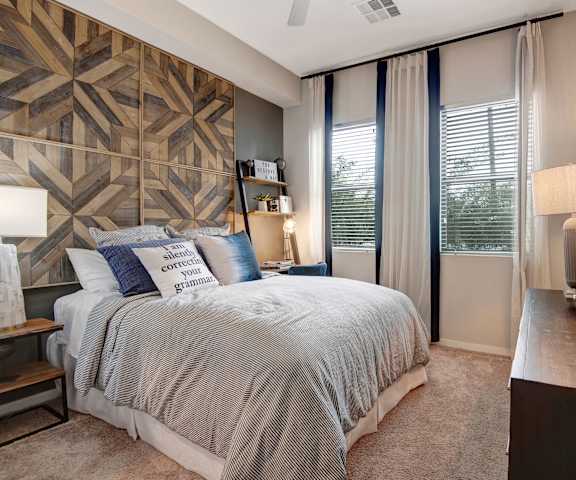 A cozy bedroom with a queen-size bed, wall art, a cactus, a dresser, decorations, window, and nightstands at Park on Central Apartments.