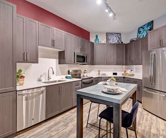 A large kitchen with stainless steel appliances, spacious white marble countertops, and large wooden cabinets at Park on Central Apartments. 