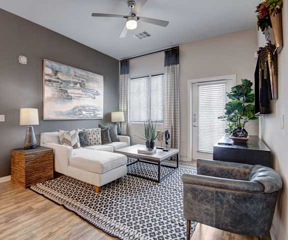 The living room with a white couch, wall art, plush chairs, coffee table, windows, decorations, a TV, and balcony at Park on Central Apartment Homes. 