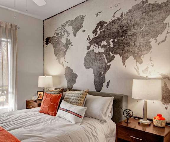 A cozy bedroom with a queen-size bed with orange accents, a dresser, decorations, window, a tan and brown map of the world, and nightstands at