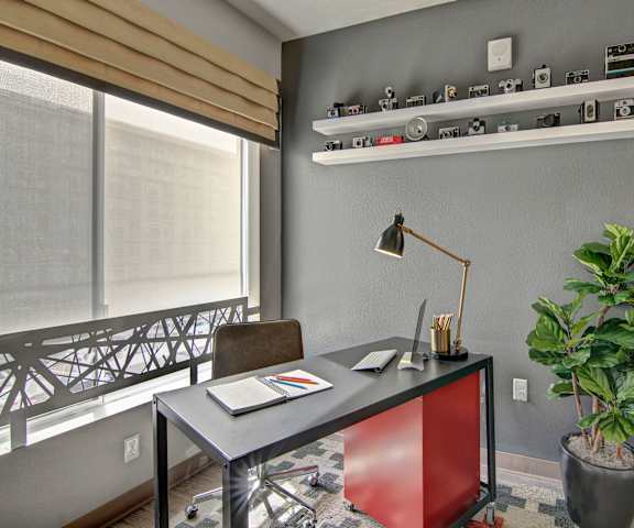 The office with a desk, chair, lamp, plant, wall art, and large window with gray walls at Proxy 333 Apartment Homes. 