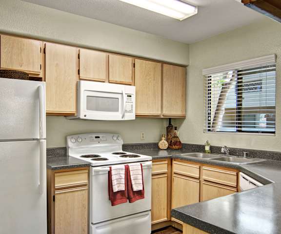 A cozy kitchen with white appliances, a light counter with lots of room, and spacious wooden cabinets at Reserve at Arrowhead Apartment Homes. 