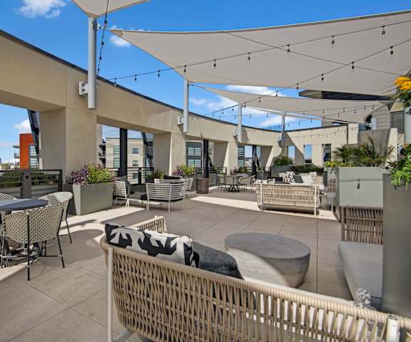Roosevelt Row Outdoor Area The rooftop balcony lounge with wicker couches and chairs, coffee tables, potted plants, and string lights below a canopy cover at Roosevelt Row Apartment Homes.
