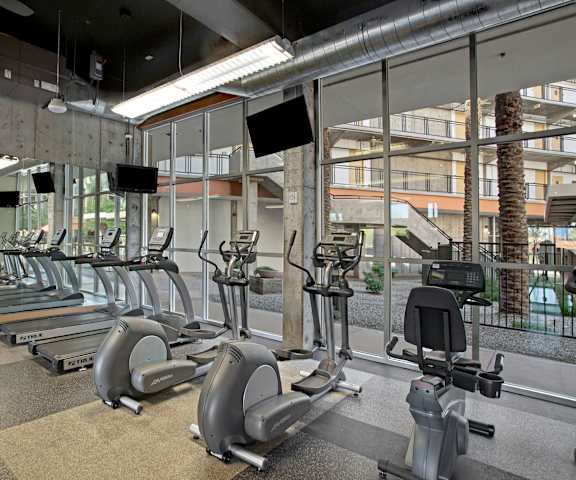 A spacious gym with cardio machines, windows, TVs, and weights at Skyline Lofts Apartment Homes. 